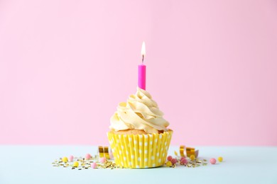 Photo of Delicious birthday cupcake with burning candle and sprinkles on white table against pink background