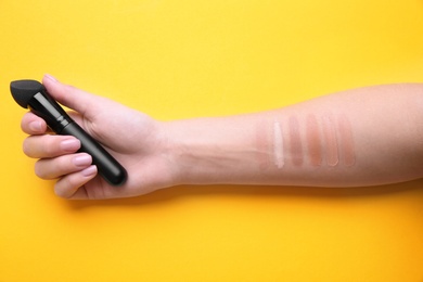 Photo of Woman testing different shades of liquid foundation on her hand against color background, closeup