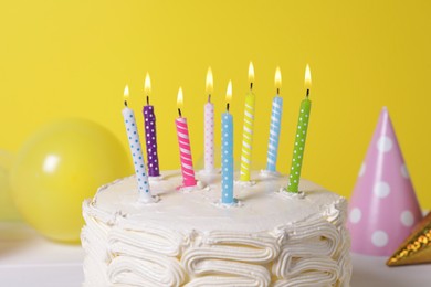 Photo of Delicious cake with burning candles and festive decor on yellow background, closeup