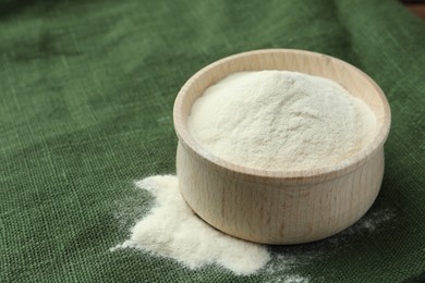 Wooden bowl of agar-agar powder on green tablecloth, closeup. Space for text