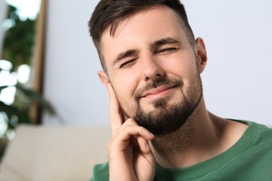 Photo of Young man suffering from ear pain at home. Space for text