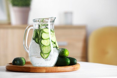 Refreshing cucumber water with rosemary in jug and vegetables on white table. Space for text