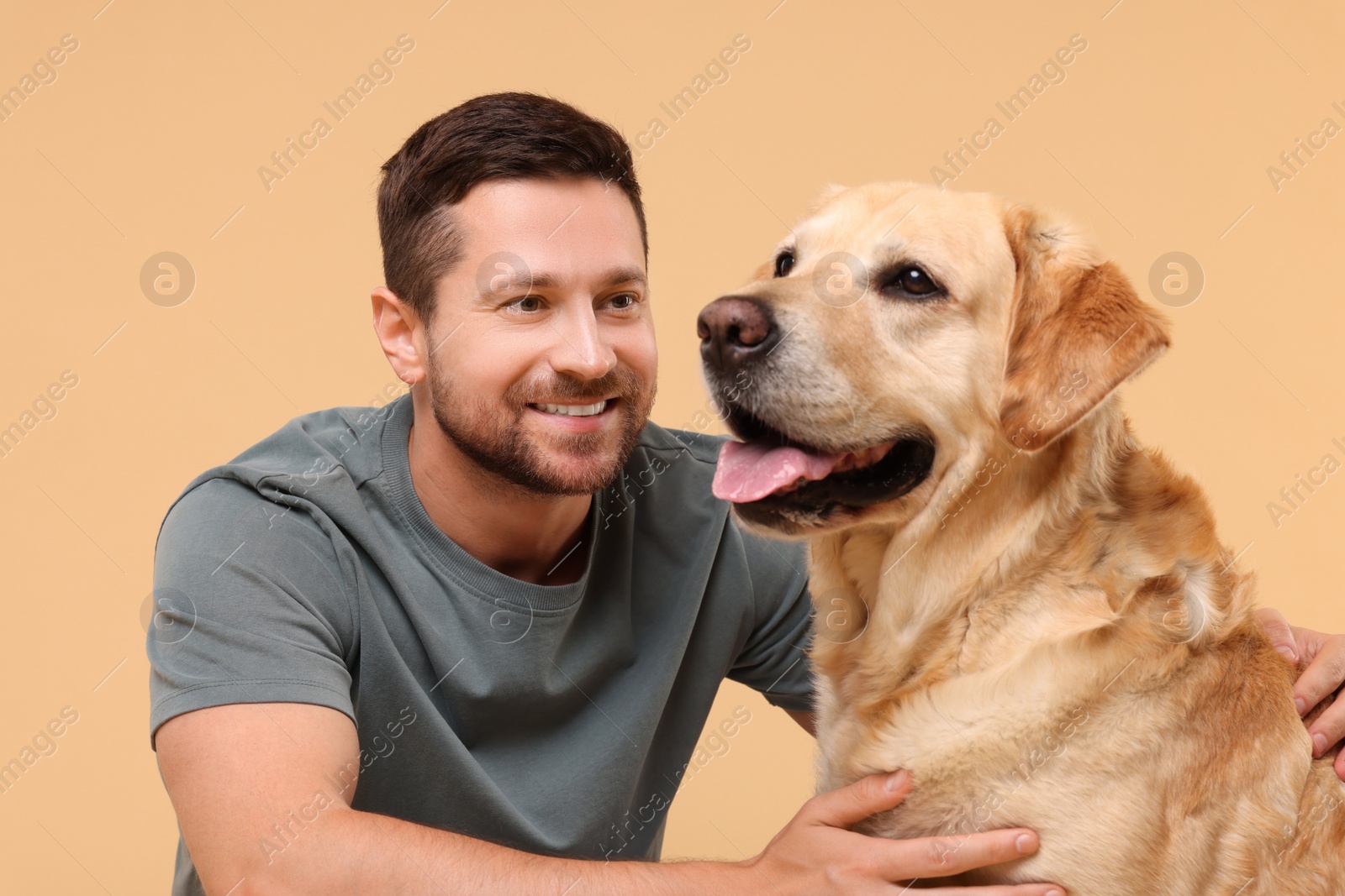 Photo of Man hugging with adorable Labrador Retriever dog on beige background. Lovely pet