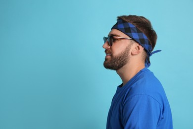 Photo of Fashionable young man in stylish outfit with bandana on light blue background, space for text