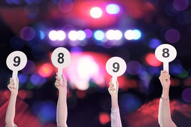 Panel of judges holding signs with different score against blurred background, closeup. Bokeh effect