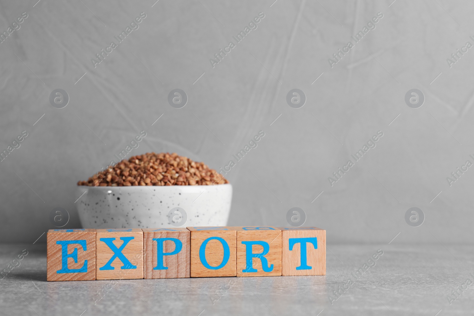 Photo of Word Export made of wooden cubes and bowl with buckwheat grains on grey background. Space for text