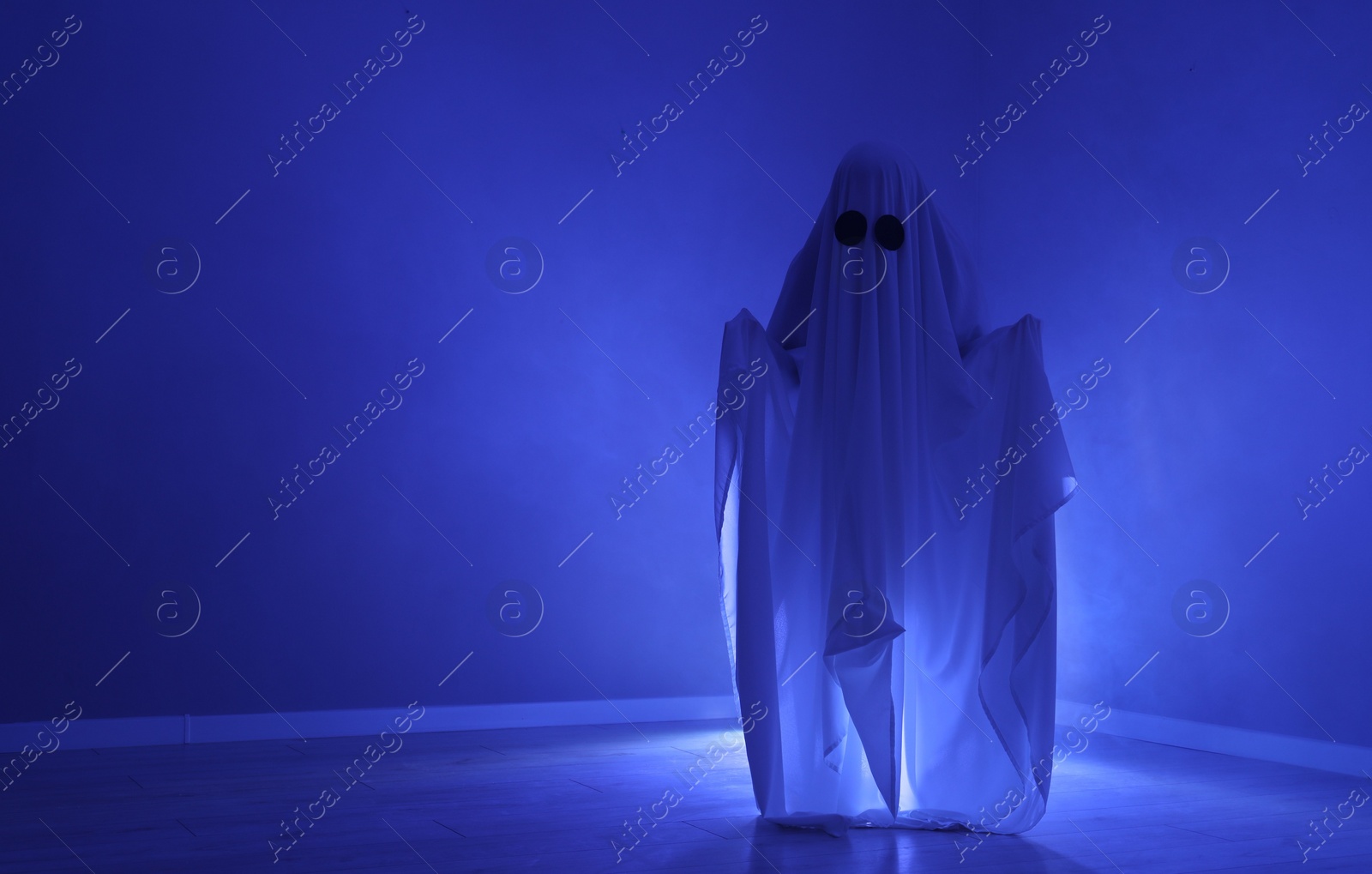 Photo of Creepy ghost. Woman covered with sheet in blue light, space for text