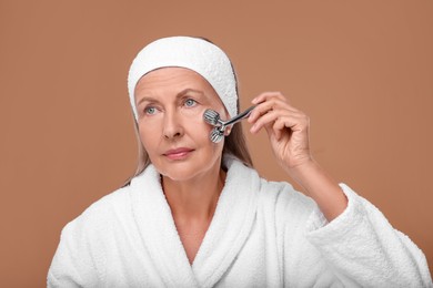 Woman massaging her face with metal roller on brown background