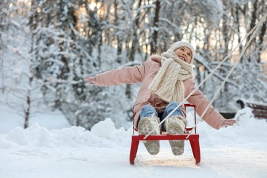 Cute little girl enjoying sledge ride through snow in winter park