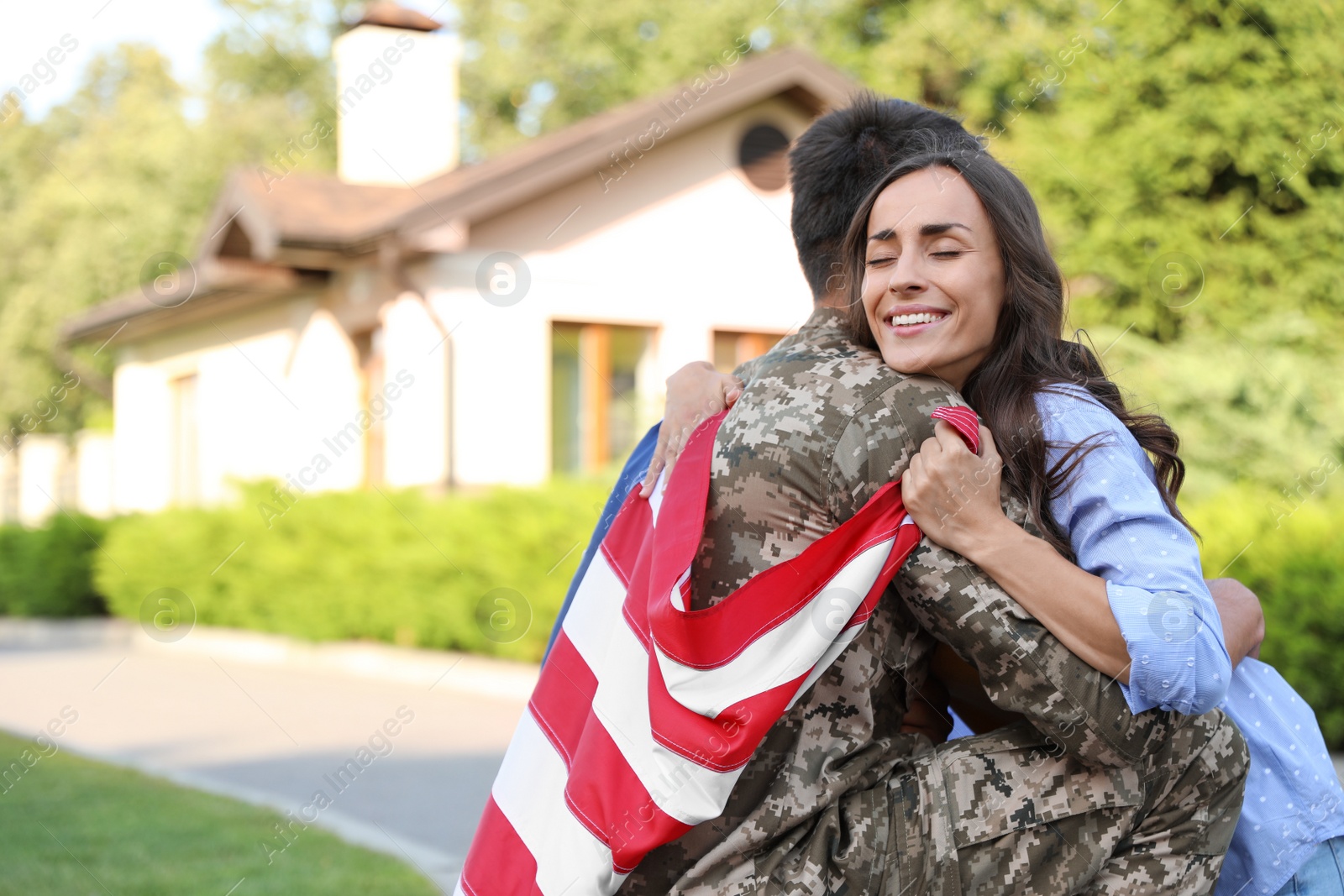 Photo of Man in military uniform with American flag hugging his wife outdoors