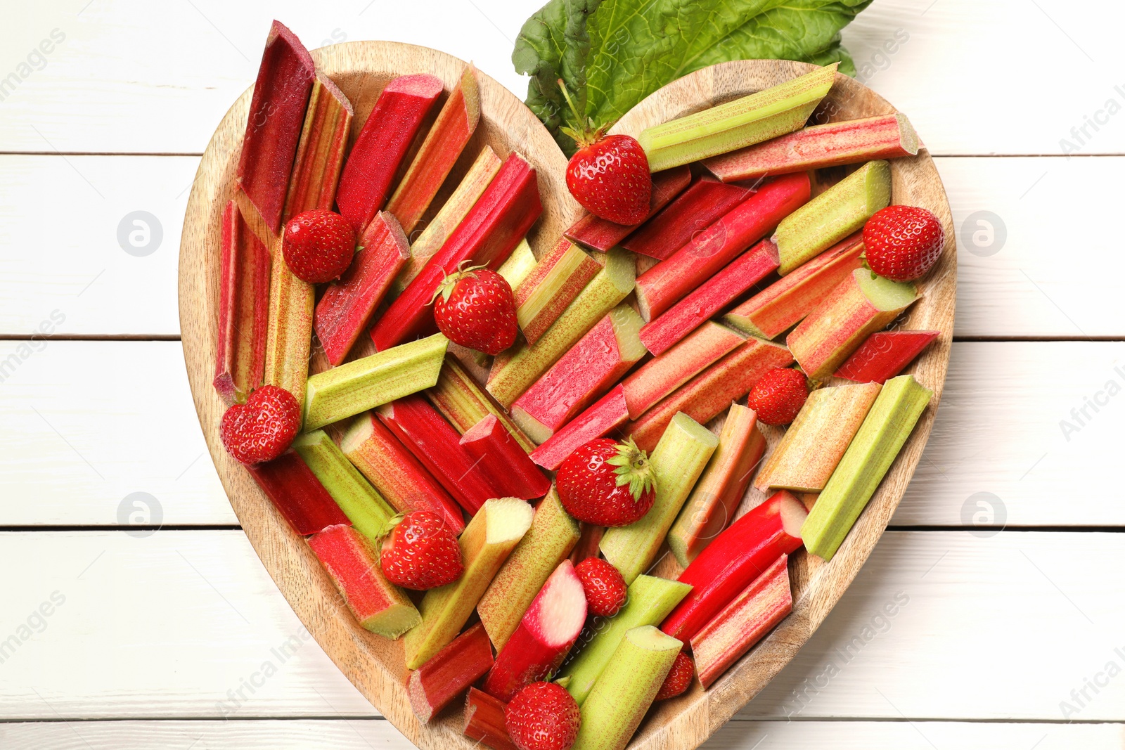Photo of Cut fresh rhubarb stalks and strawberries on white wooden table, top view