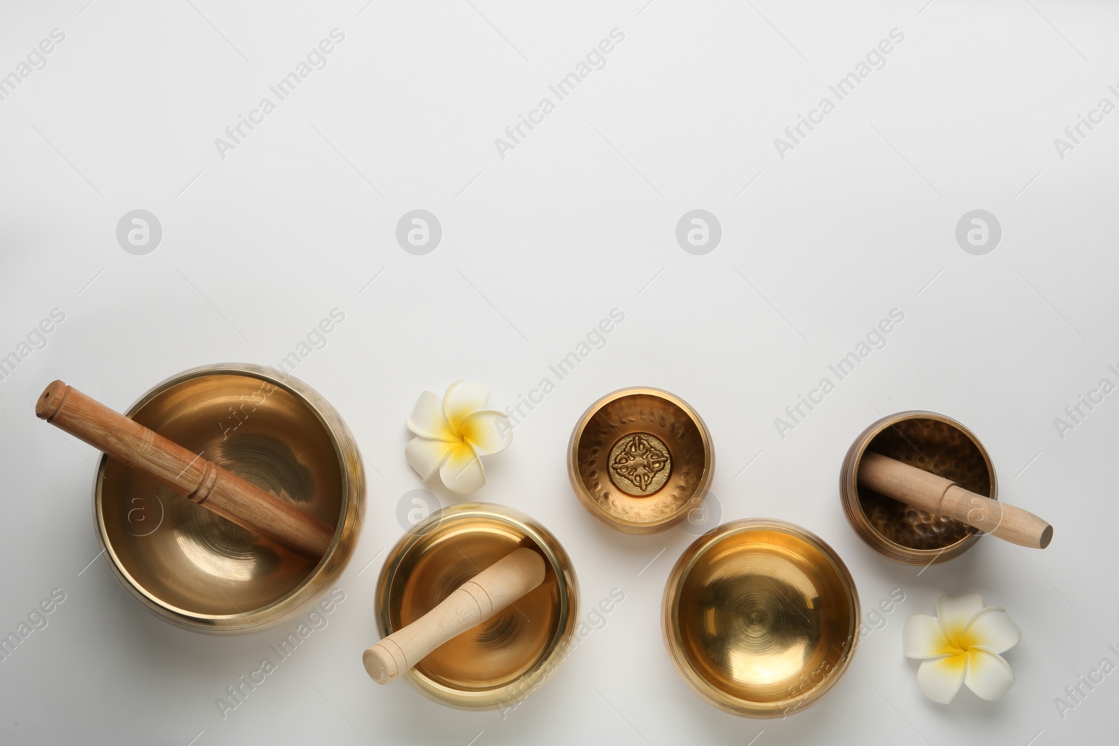 Photo of Golden singing bowls, mallets and flowers on white background, flat lay. Space for text