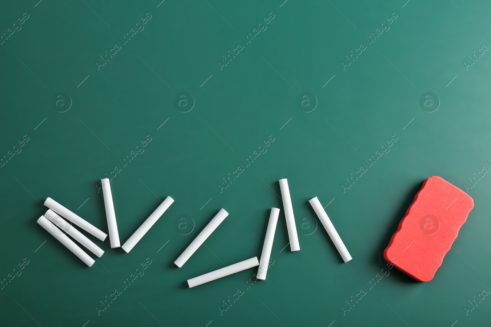 Photo of Pieces of chalk and blackboard duster on green background, top view