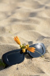 Stylish sunglasses and tropical flower on sand, closeup. Space for text