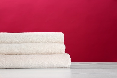 Photo of Stack of soft clean towels on table against color background. Space for text