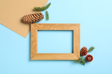 Pinecones, fir branches and wooden frame on color background, flat lay. Space for text