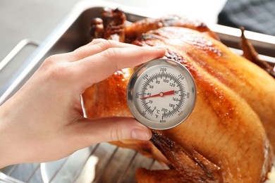 Photo of Woman measuring temperature of whole roasted turkey with meat thermometer, closeup