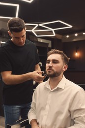 Professional hairdresser working with client in barbershop