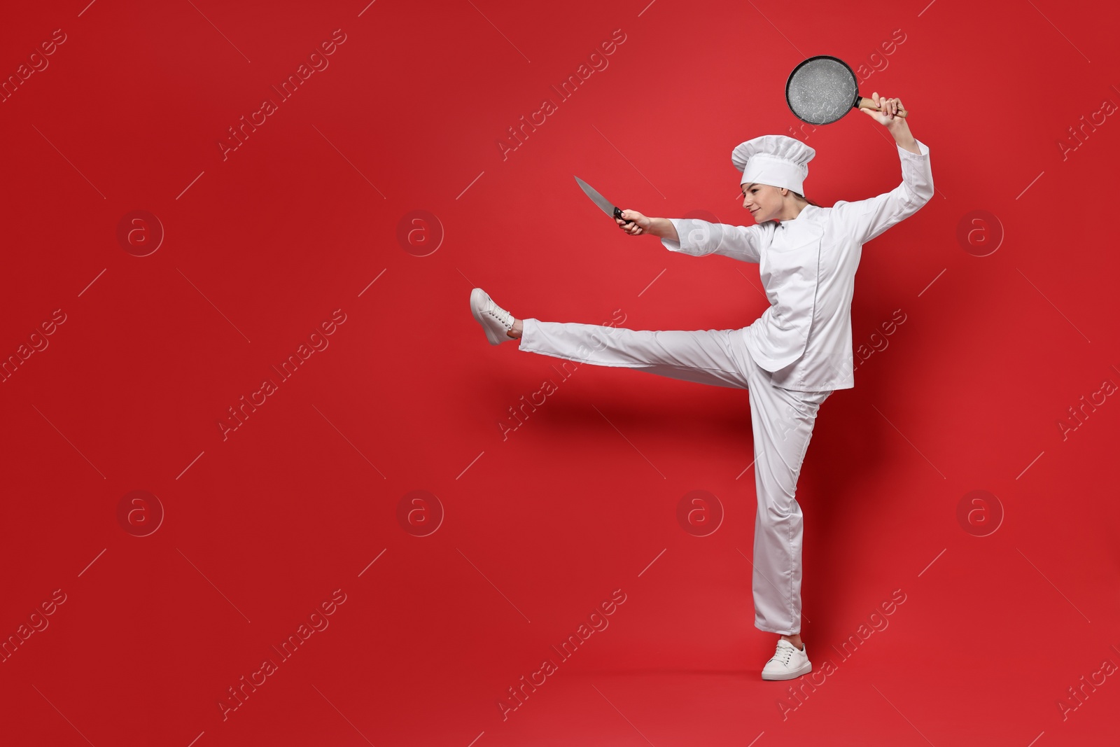 Photo of Professional chef with frying pan and knife having fun on red background. Space for text