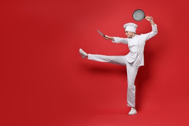 Photo of Professional chef with frying pan and knife having fun on red background. Space for text