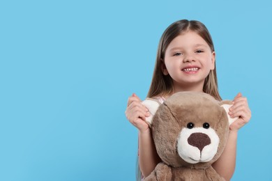 Cute little girl with teddy bear on light blue background. Space for text