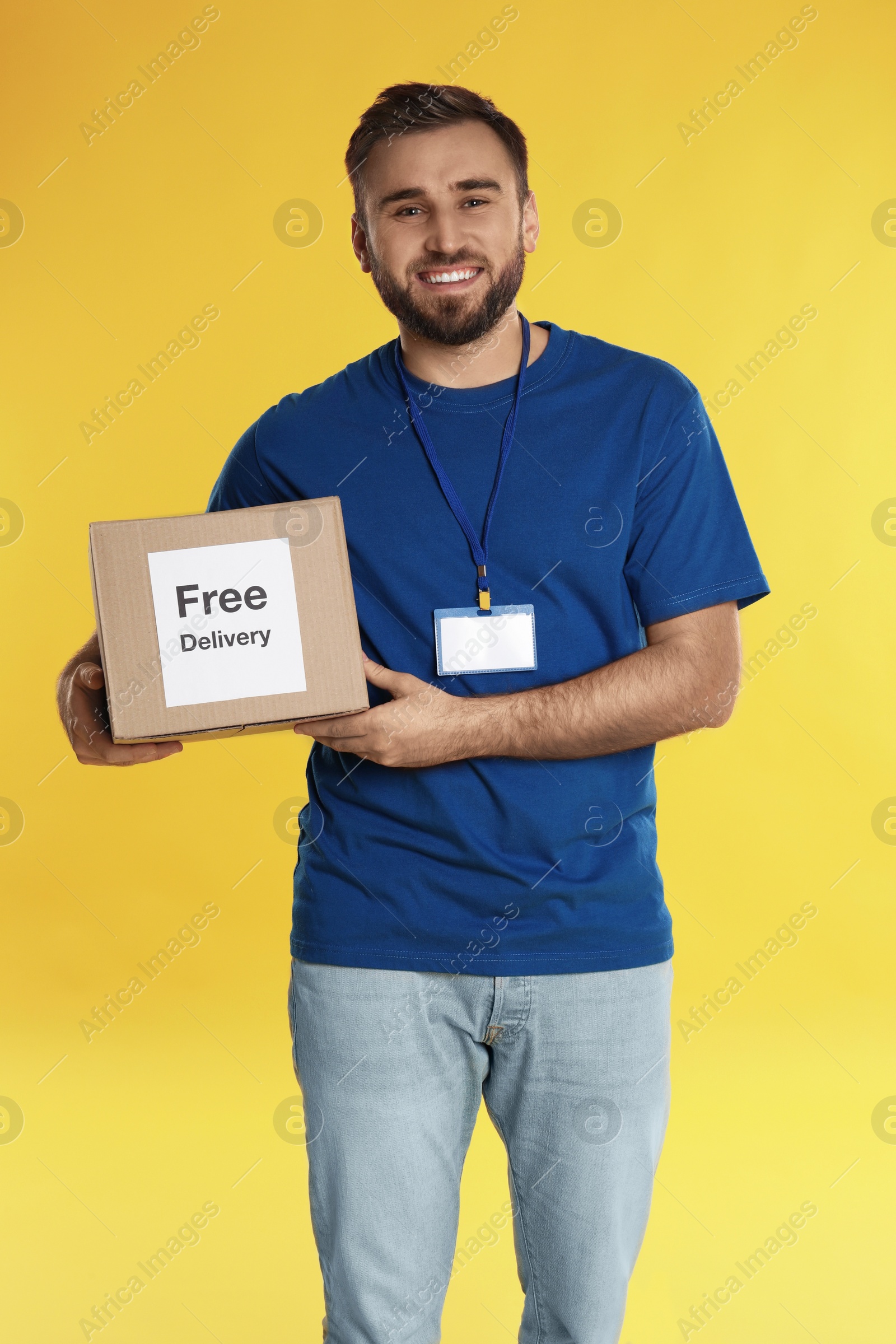 Photo of Male courier holding parcel with sticker Free Delivery on yellow background