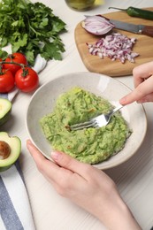 Woman preparing delicious guacamole at white wooden table, closeup