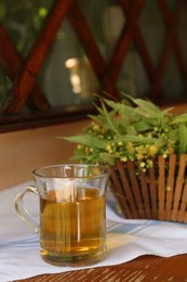 Glass cup of aromatic tea and linden blossoms on wooden table, space for text