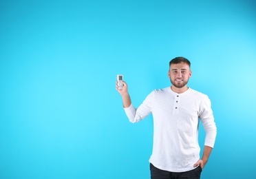 Young man with air conditioner remote on color background, copy space text