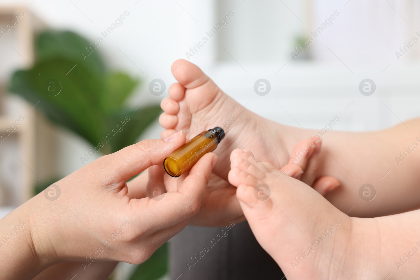 Photo of Mother applying essential oil from roller bottle onto her baby`s heel indoors, closeup