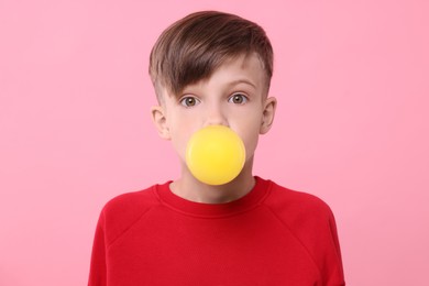 Photo of Surprised boy blowing bubble gum on pink background