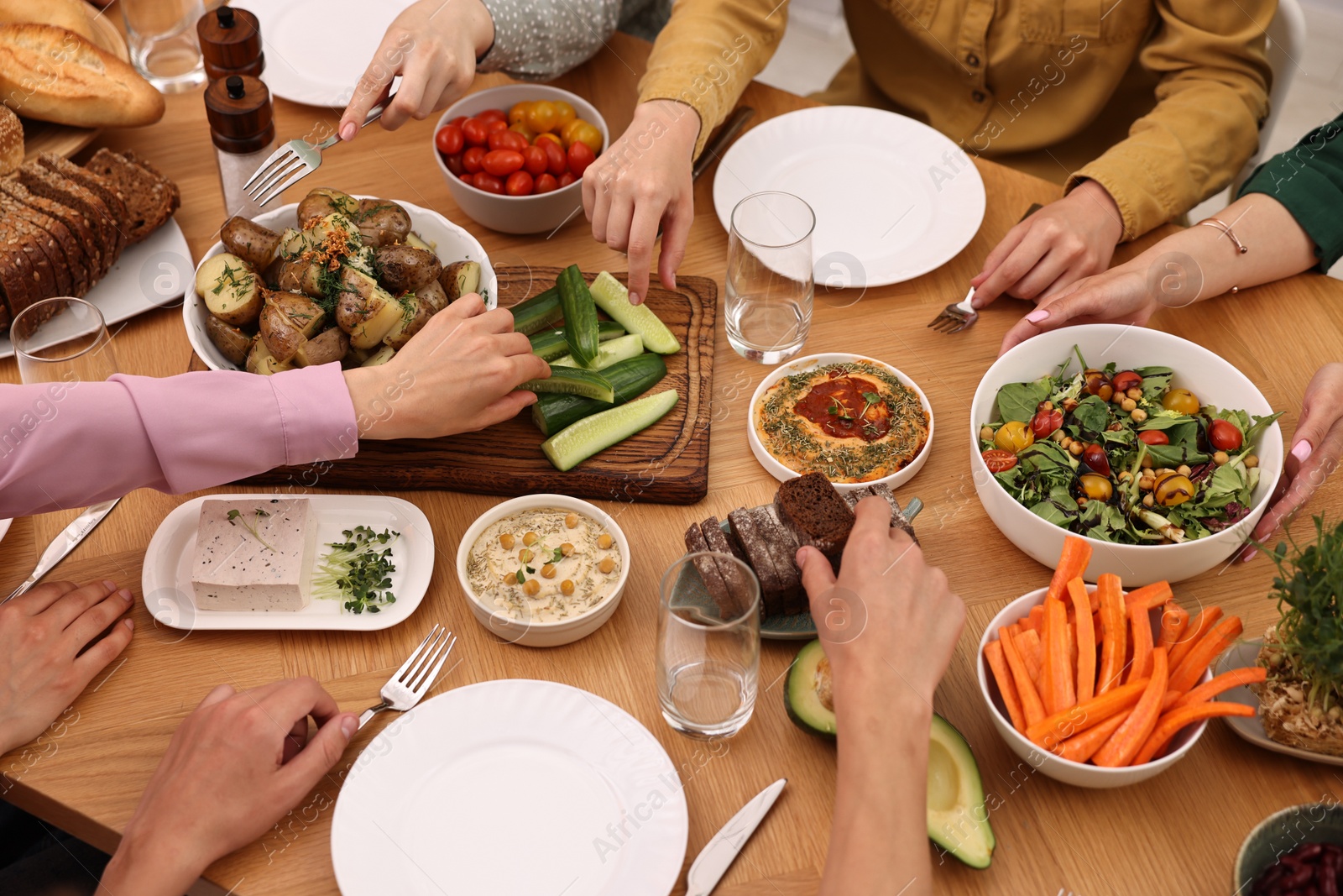 Photo of Friends eating vegetarian food at wooden table indoors, closeup