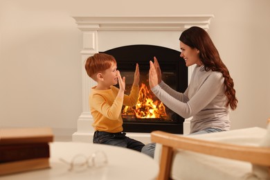 Photo of Happy mother and son playing together near fireplace at home