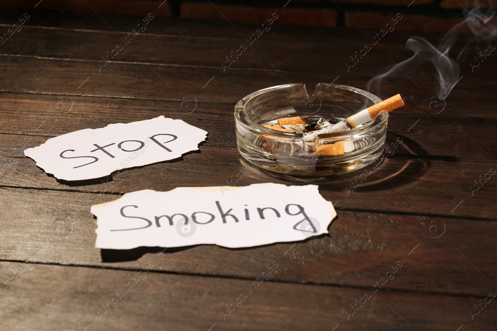 Photo of Ashtray with burnt cigarettes and words Stop Smoking written on paper on wooden table