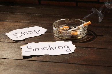 Ashtray with burnt cigarettes and words Stop Smoking written on paper on wooden table