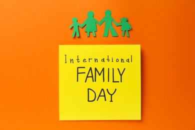 Photo of Paper cutout and card with text International Family Day on orange background, flat lay