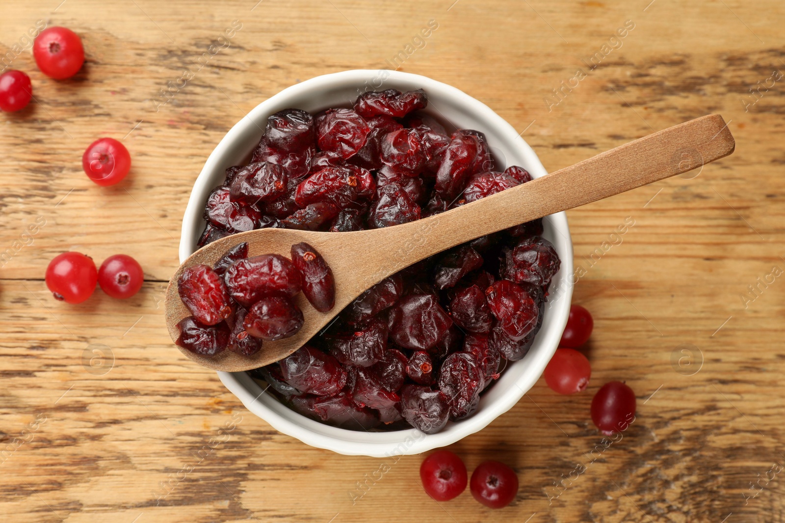 Photo of Tasty dried cranberries in bowl and fresh ones on wooden table, top view