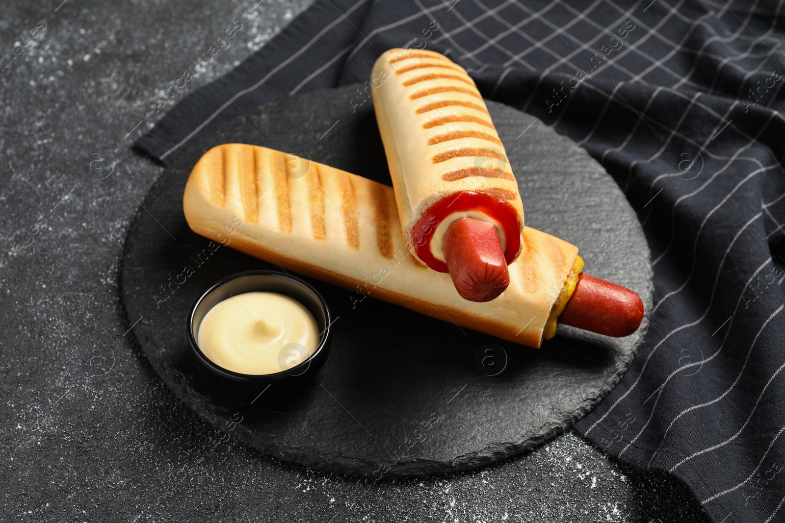 Photo of Tasty french hot dogs and dip sauce on black table