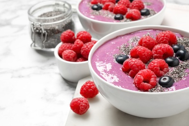 Delicious acai smoothie with raspberries and chia seeds in bowl on white marble table, closeup