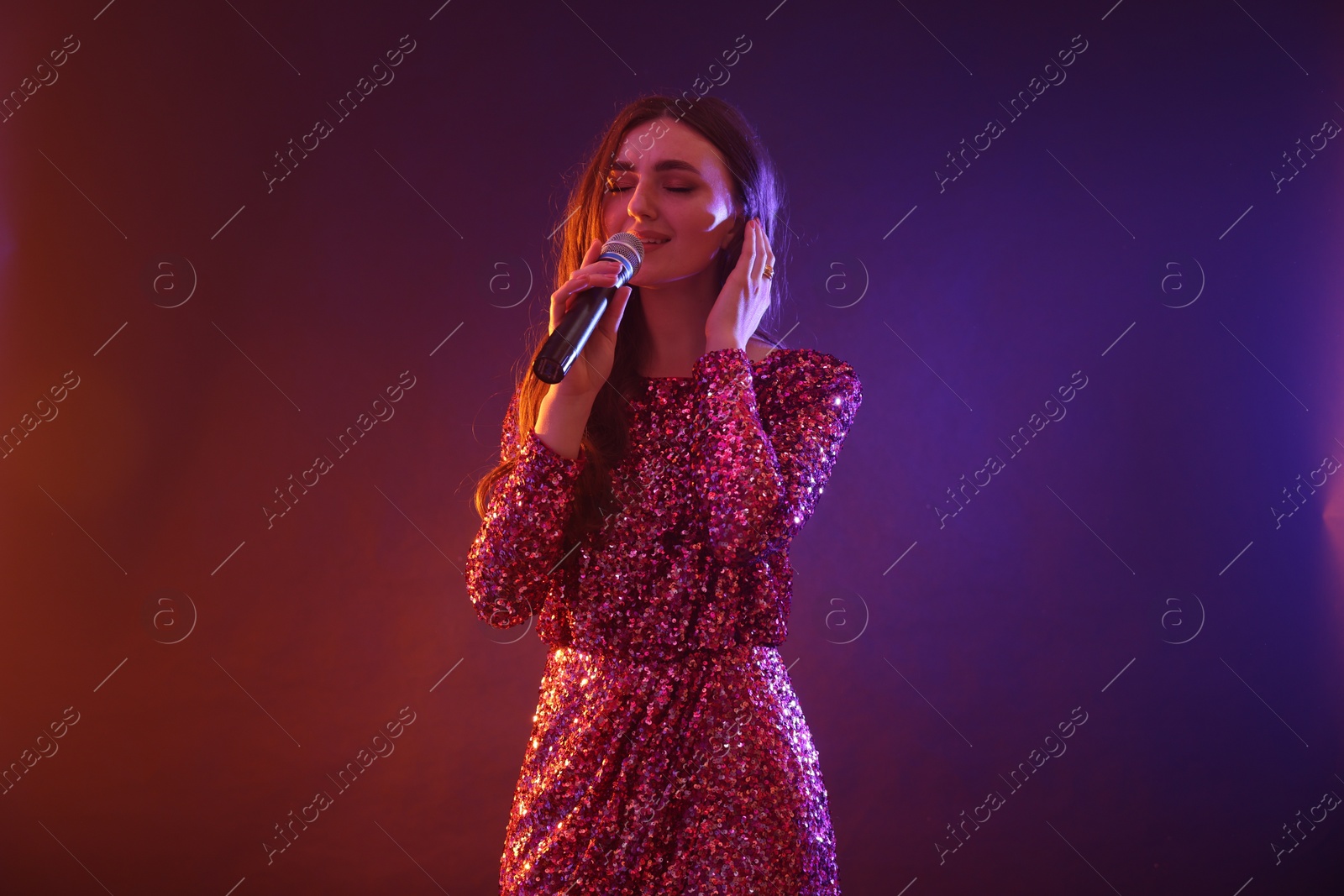 Photo of Emotional woman with microphone singing on bright background