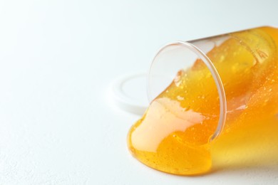 Photo of Overturned plastic container with orange slime on white background, closeup. Space for text