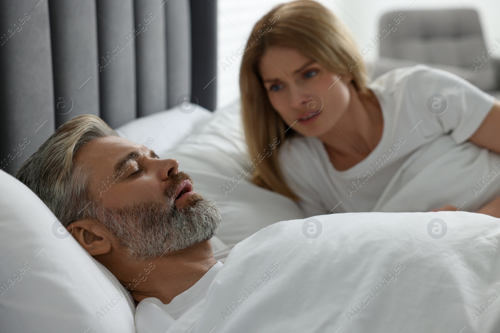 Photo of Irritated woman near her snoring husband in bed at home