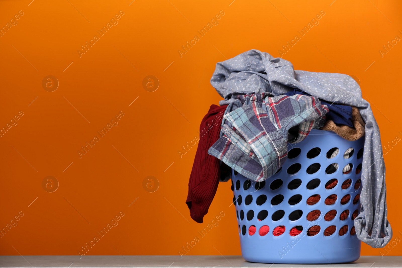 Photo of Laundry basket with clothes near orange wall. Space for text