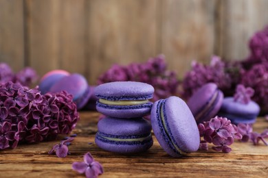 Photo of Delicious purple macarons and lilac flowers on wooden table