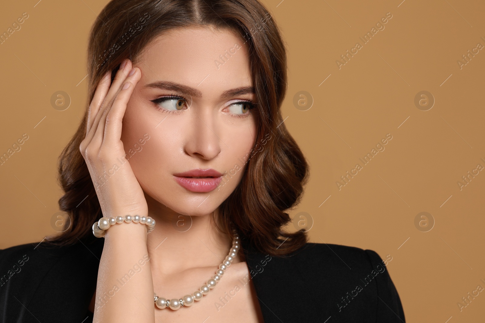 Photo of Young woman wearing elegant pearl jewelry on brown background, space for text