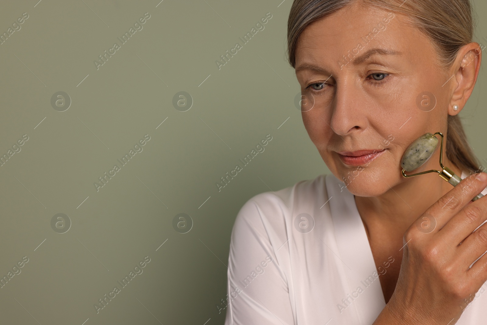 Photo of Woman massaging her face with jade roller on green background. Space for text