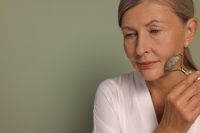 Woman massaging her face with jade roller on green background. Space for text