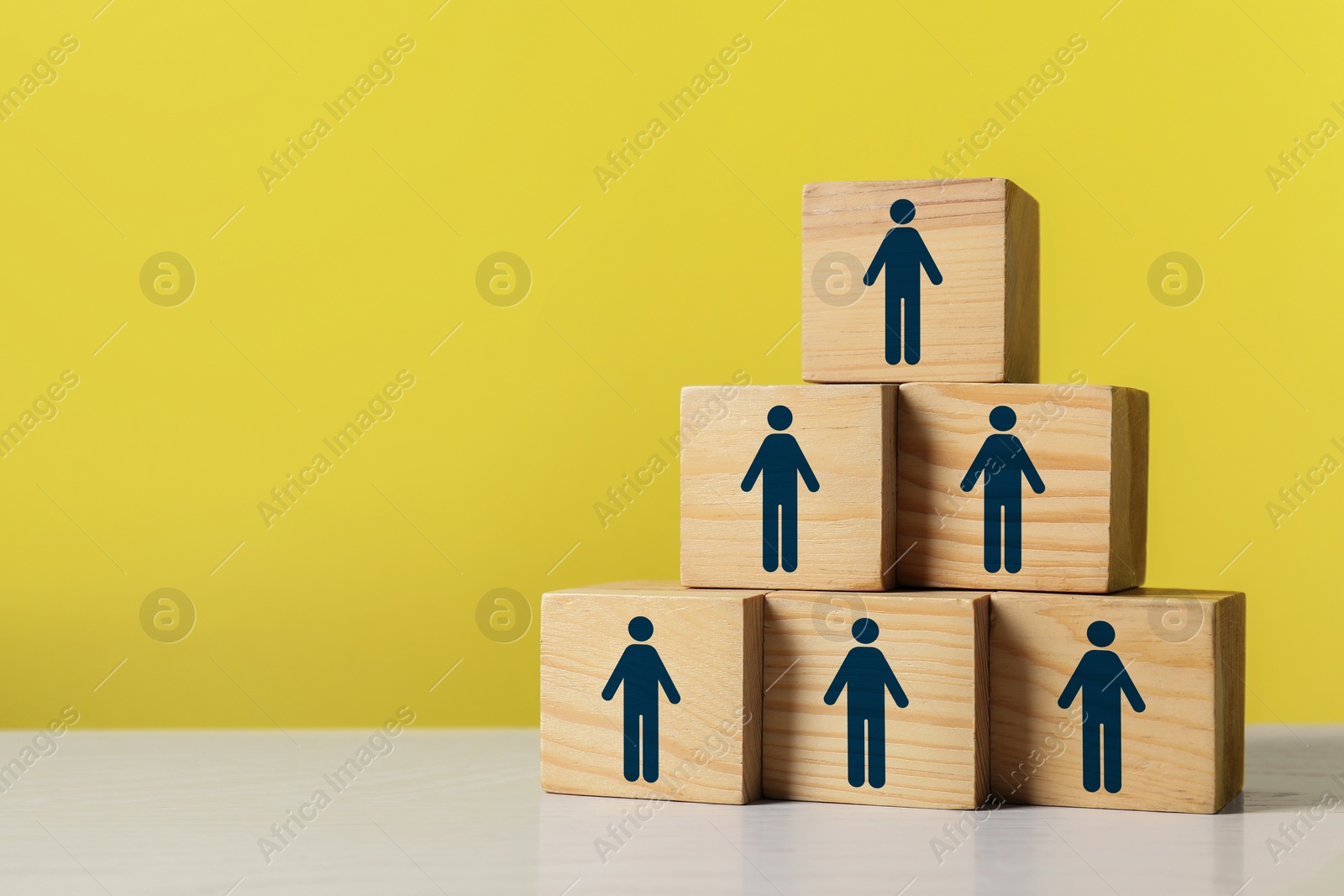 Image of Team and management concept. Pyramid of wooden cubes with human icons on white table against yellow background, space for text