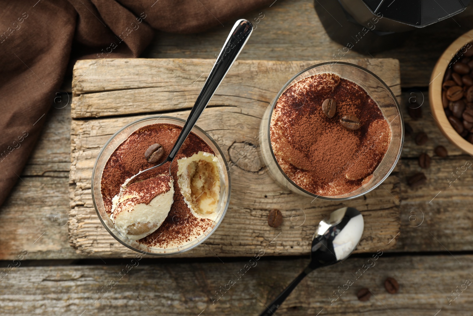 Photo of Delicious tiramisu in glasses, spoons and coffee beans on wooden table, top view