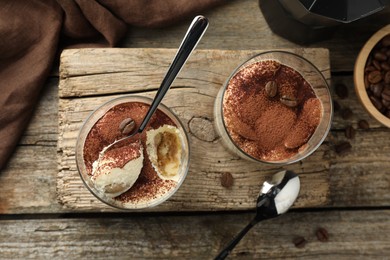 Delicious tiramisu in glasses, spoons and coffee beans on wooden table, top view